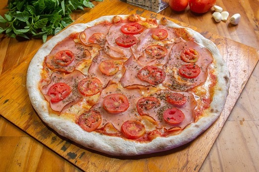 Pizza Cardinale mit Schinken und frischen Tomatenscheiben auf Holzbrett serviert